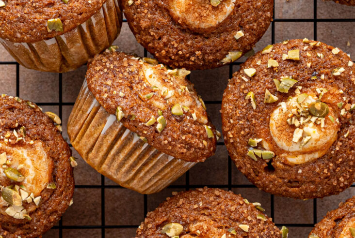 A group of golden baked Pumpkin Cream Cheese Muffins with a cream cheese, sugar, and pumpkin seed topping on a baking rack.