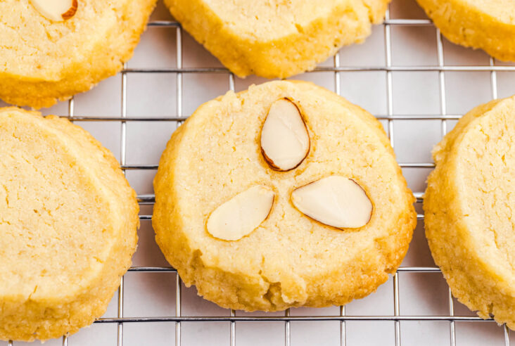 A group of Almond shortbread cookies on a cooling rack with one cookie topped with three sliced almonds.