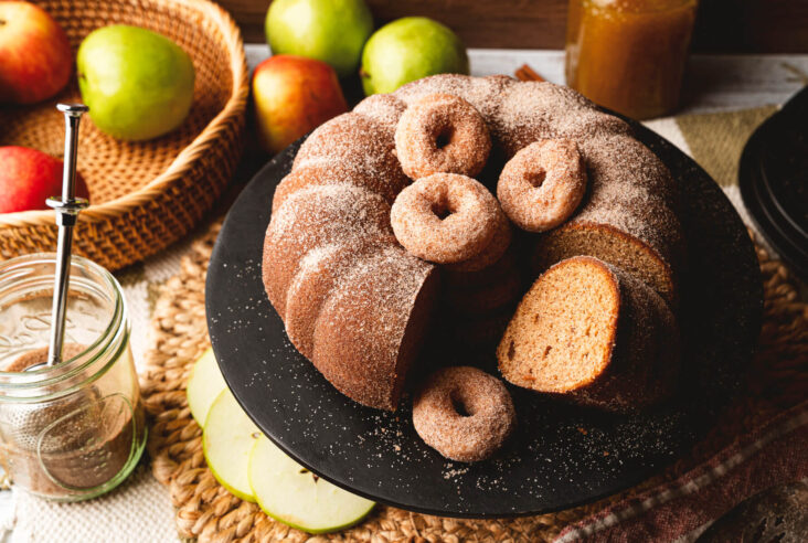 A beautiful brown Apple Cider Donut Cake with slices missing and mini donuts filling the middle hole.