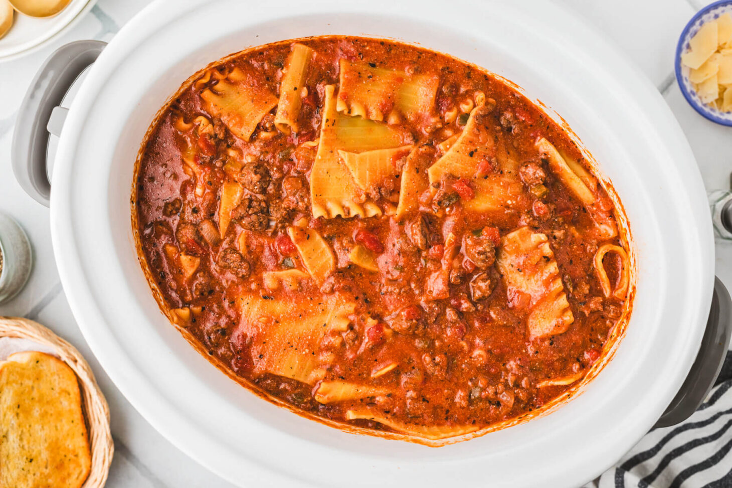 A white oval slow cooker filled with meaty lasagna soup.