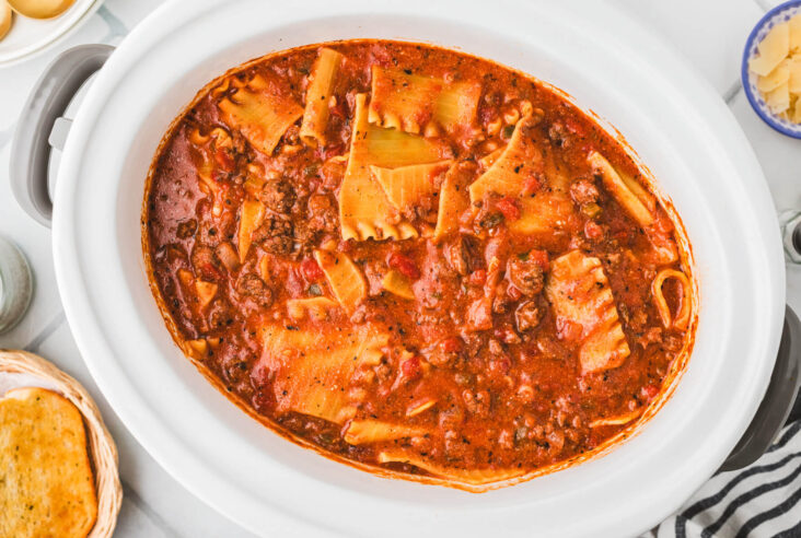 A white oval slow cooker filled with meaty lasagna soup.