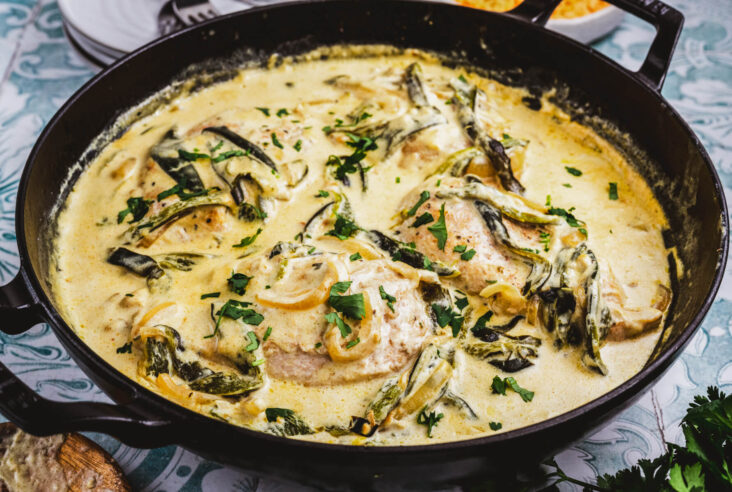 A cast iron skillet filled with roasted poblano peppers, onions, and chicken in a creamy sauce.