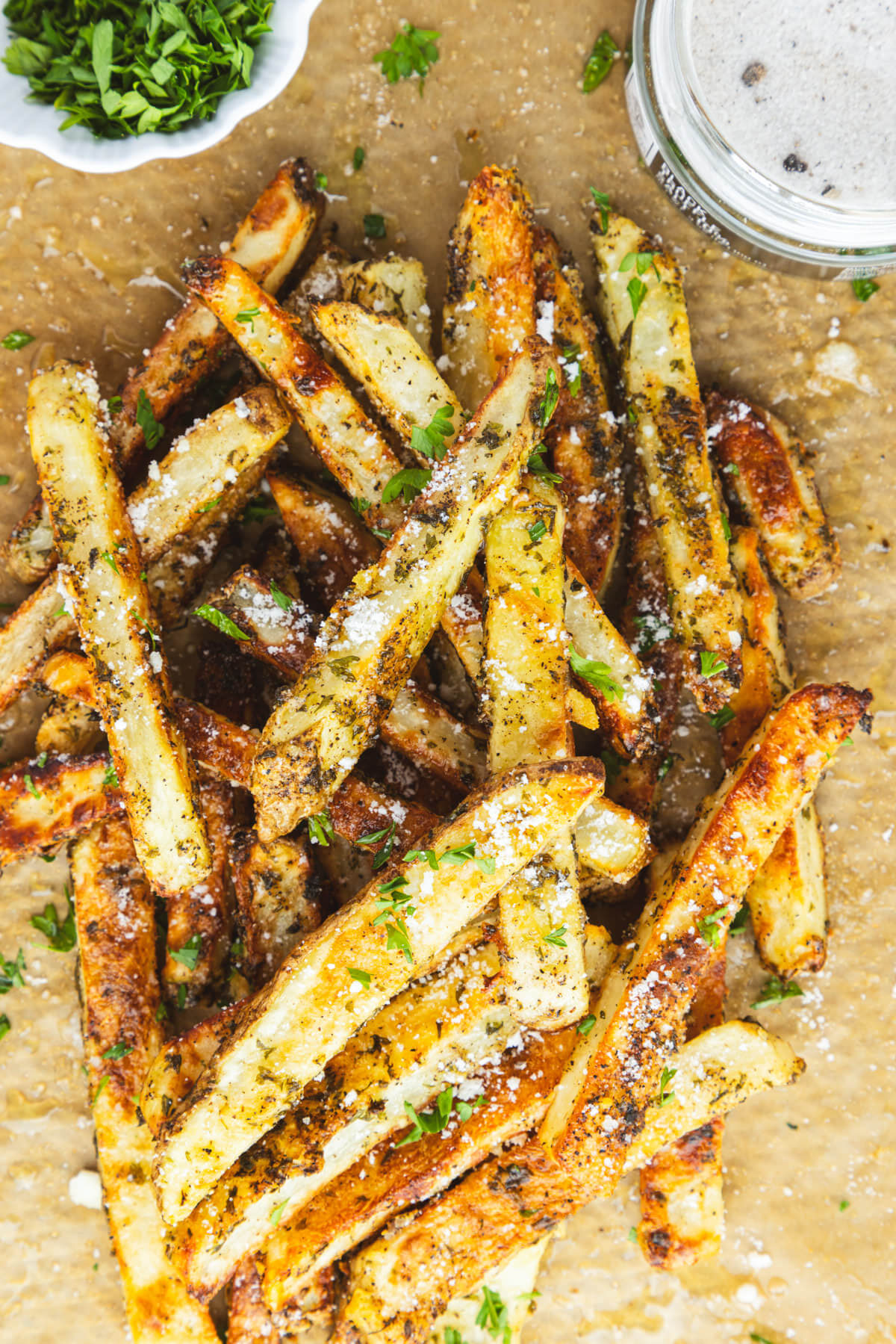 A group of golden brown oven baked truffle fries dotted with parsley and black truffle salt on butcher paper.