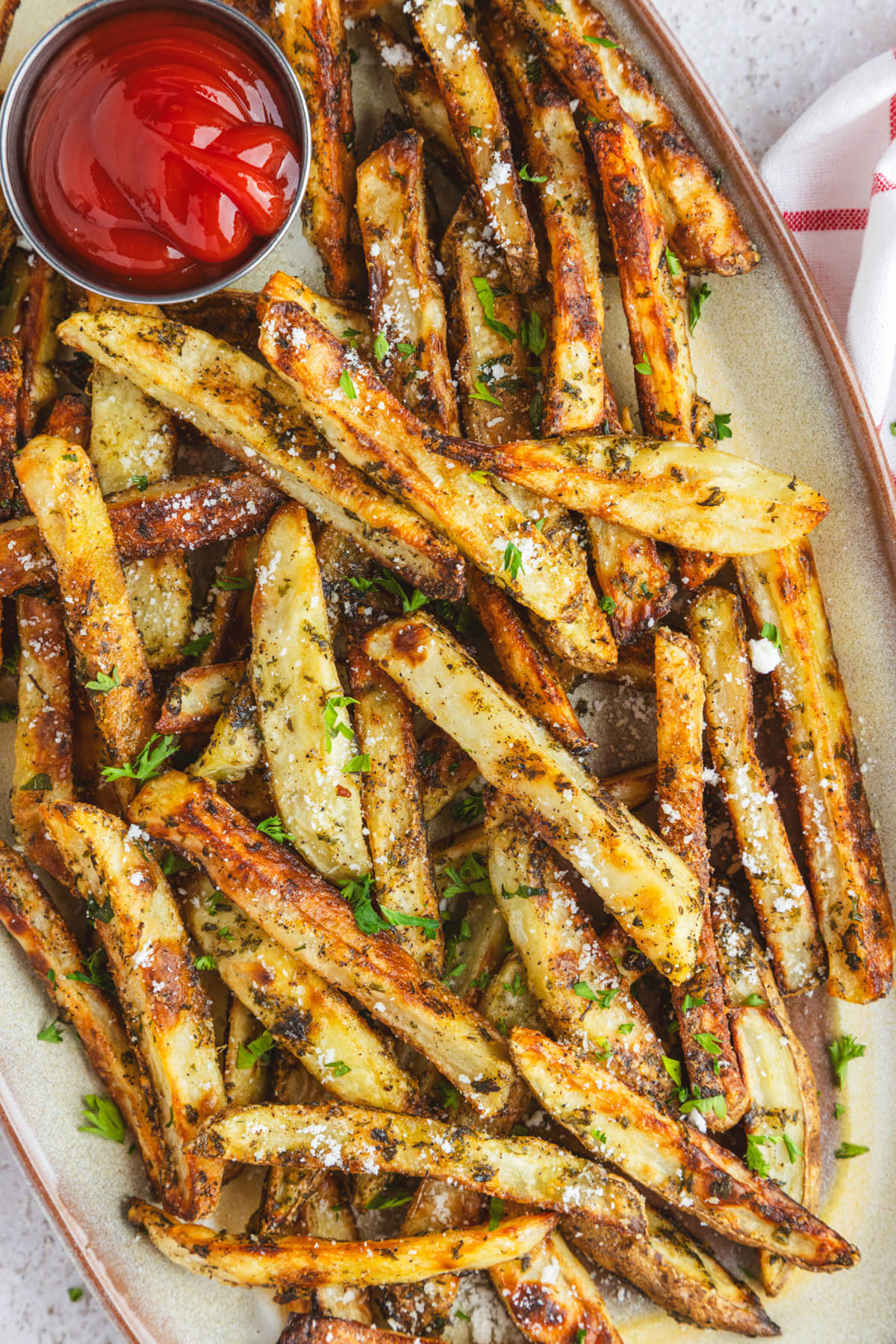 A plate of golden brown oven baked truffle fries dotted with parsley and black truffle salt with a container of ketchup.
