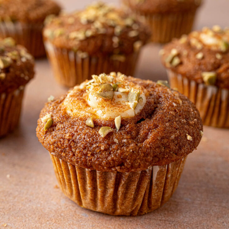 A group of golden baked Pumpkin Cream Cheese Muffins with a cream cheese, sugar, and pumpkin seed topping.
