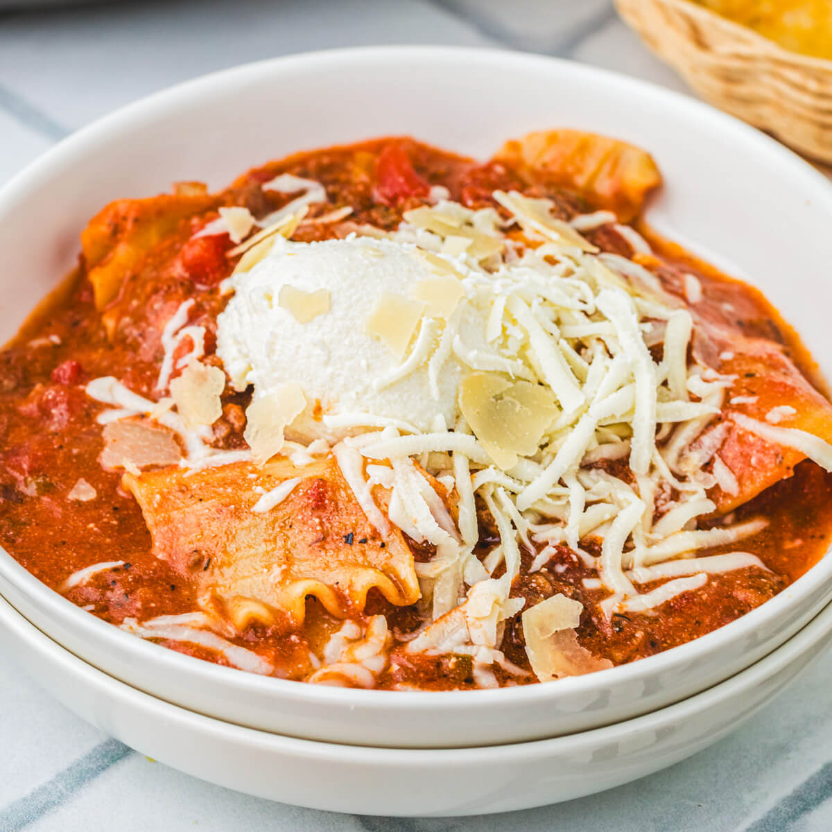 A white bowl full of Slow Cooker Lasagna soup topped with ricotta, mozzarella, and Parmesan cheese.