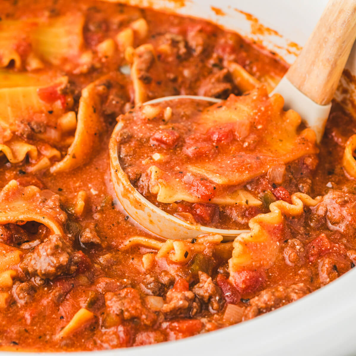 A ladle full of lasagna noodles in tomato soup broth.