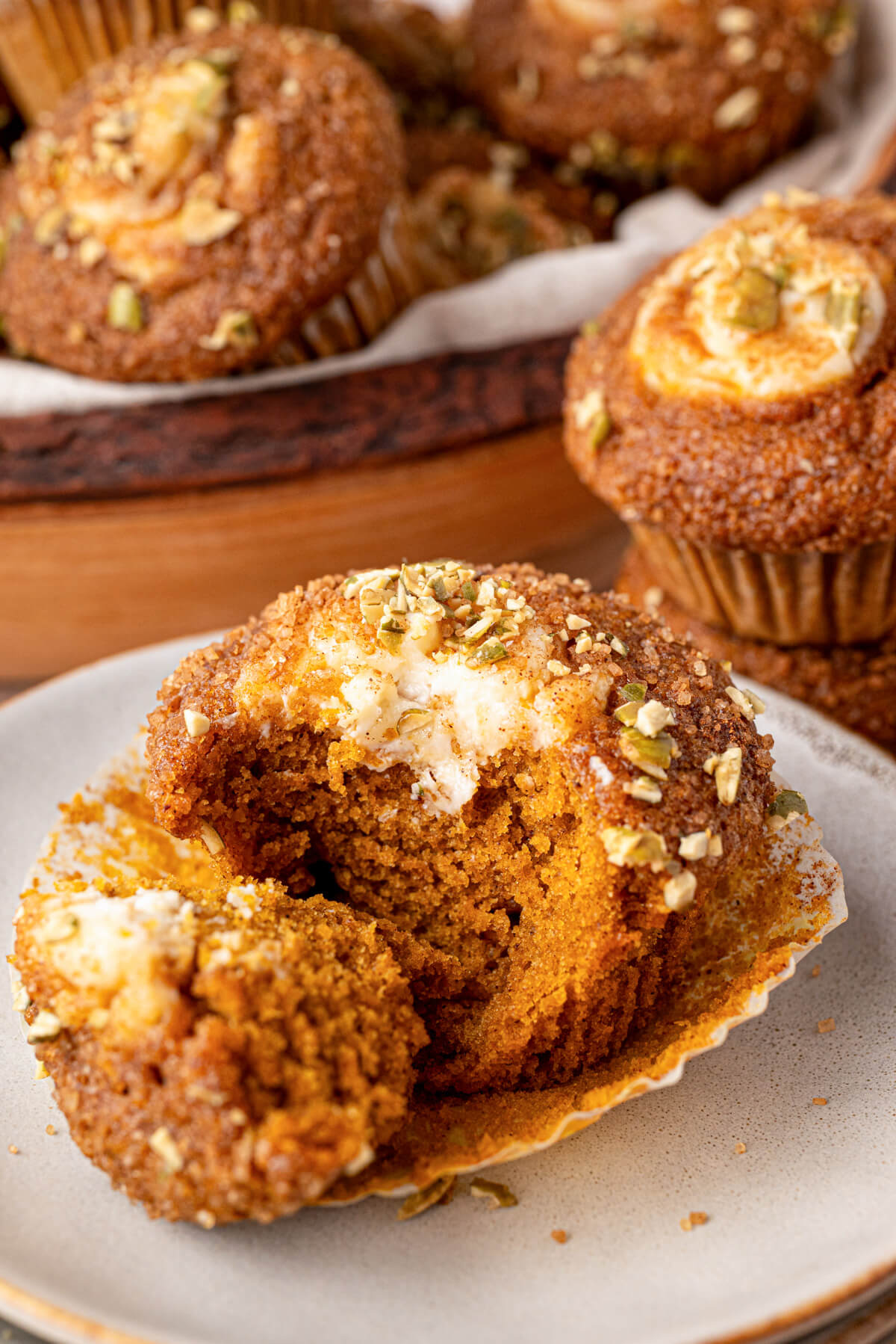 One golden baked Pumpkin Cream Cheese Muffin on a plate with the muffin paper partly removed.