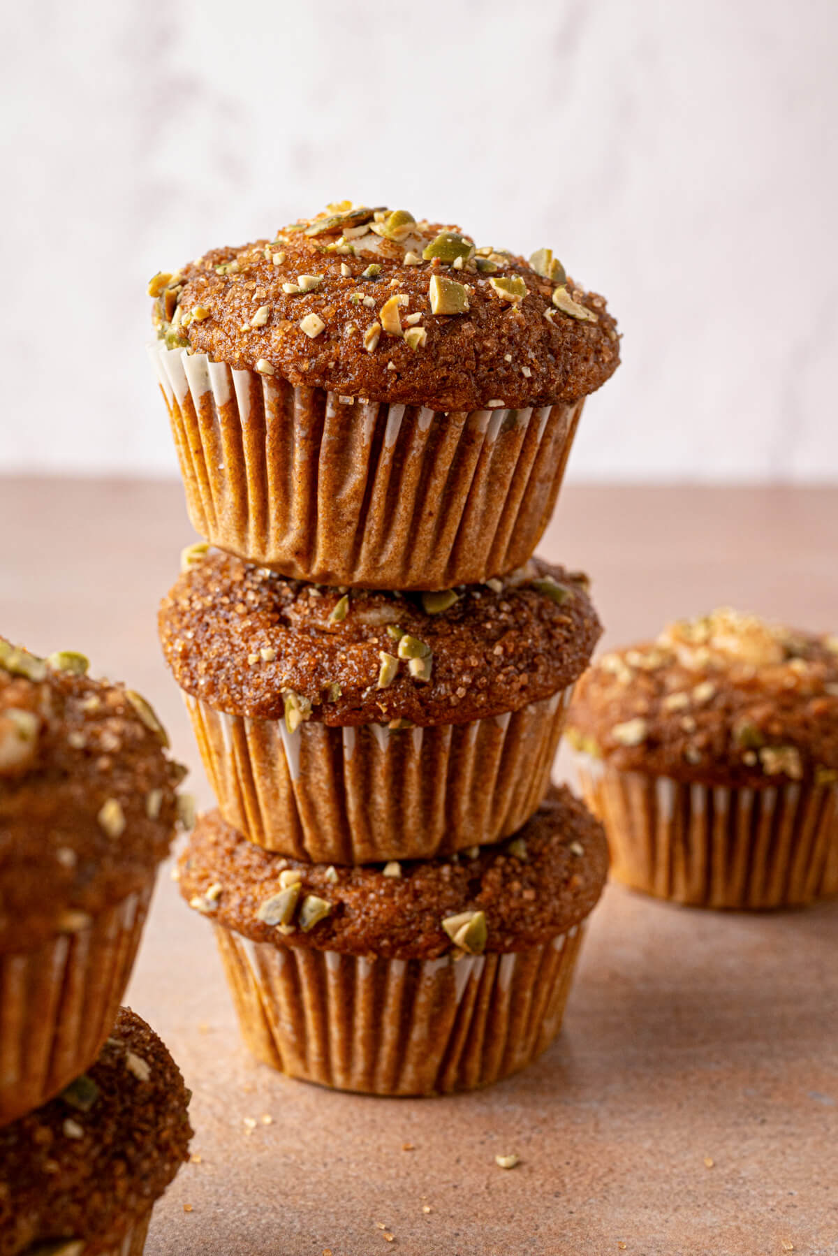 A stack of golden baked Pumpkin Cream Cheese Muffins with a cream cheese, sugar, and pumpkin seed topping.