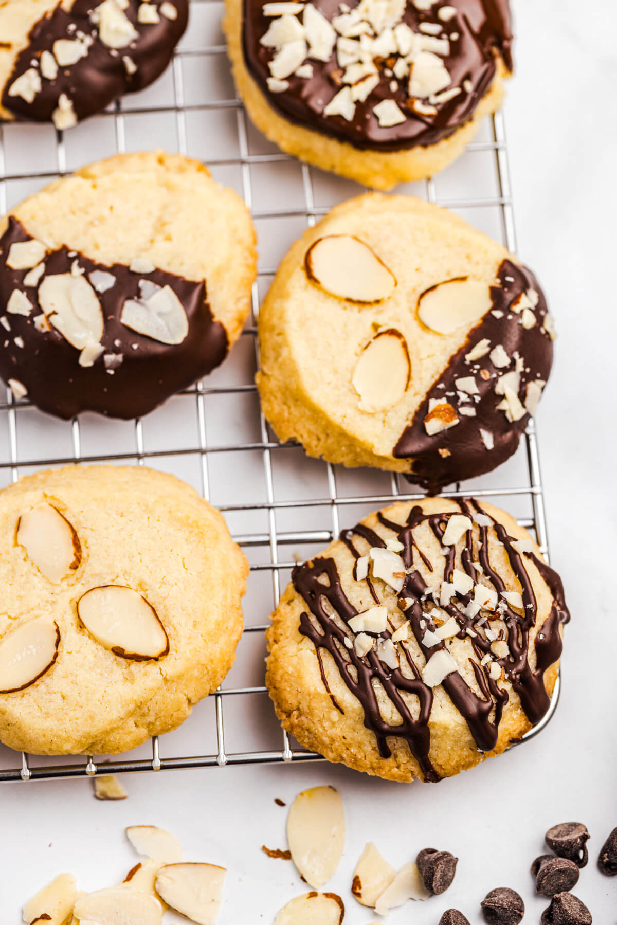 A group of almond shortbread cookies on a cooling rack decorated simply with chocolate glaze or dipped in chocolate accented with sliced and chopped almonds.