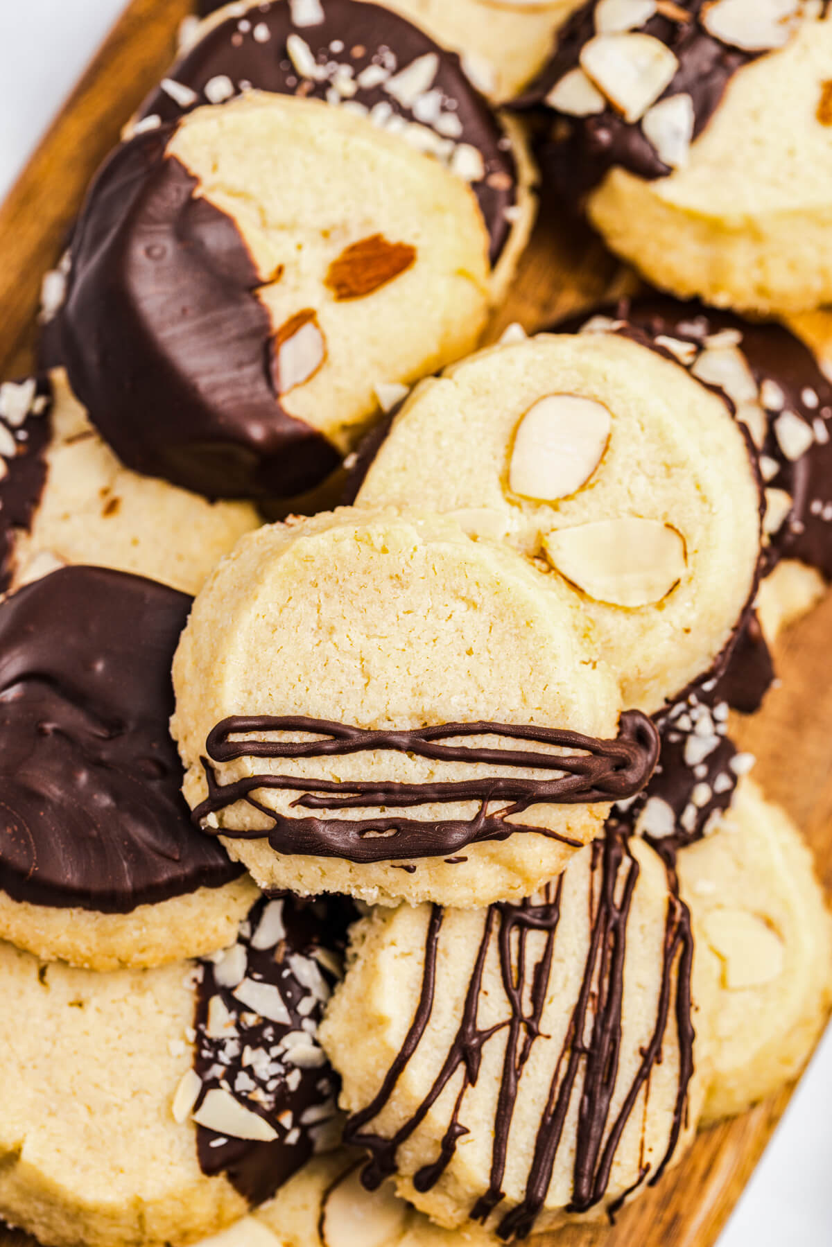 A group of almond shortbread cookies decorated simply with chocolate glaze or dipped in chocolate accented with sliced and chopped almonds on a wooden board.