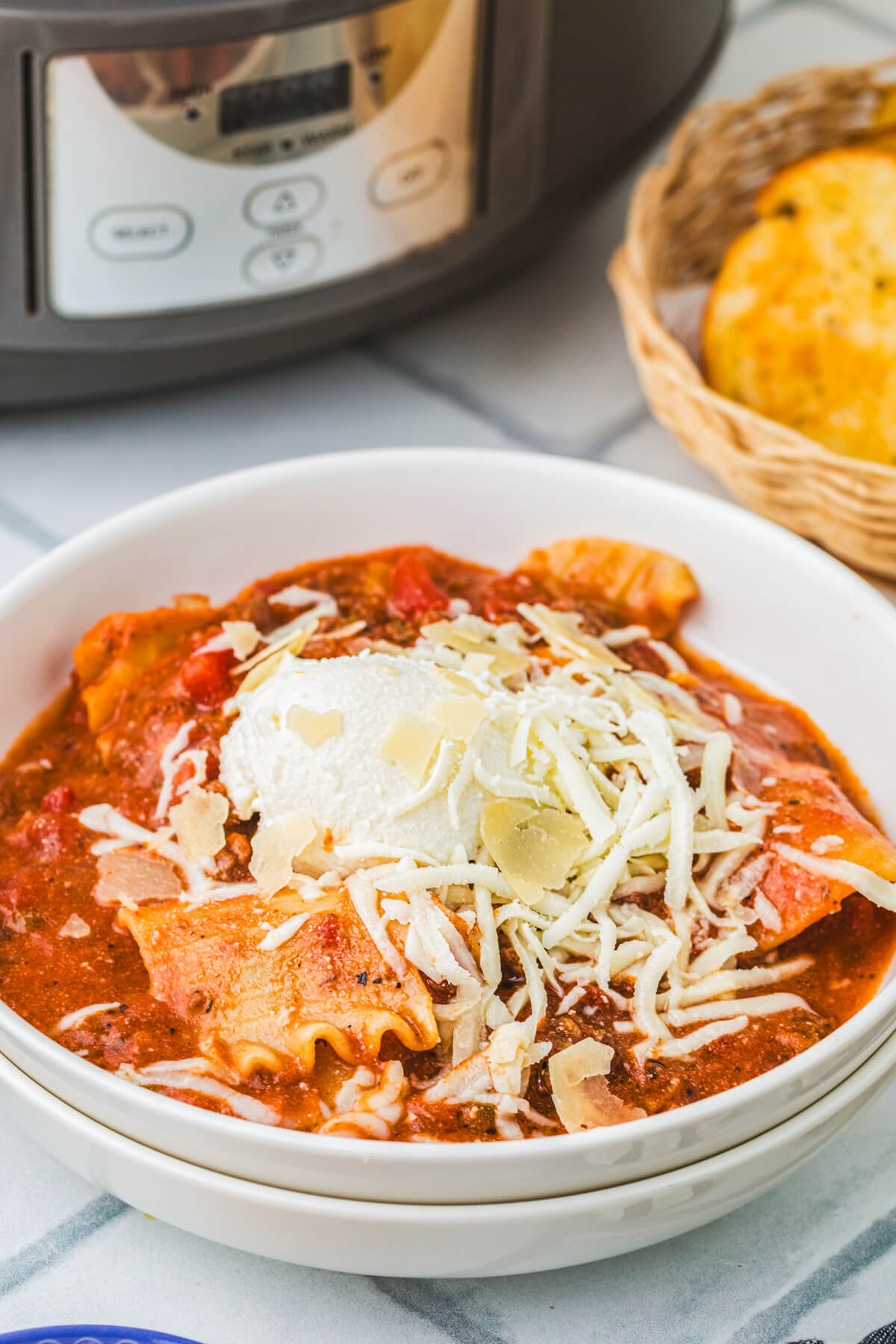 A white bowl full of Slow Cooker Lasagna soup topped with ricotta, mozzarella, and Parmesan cheese.