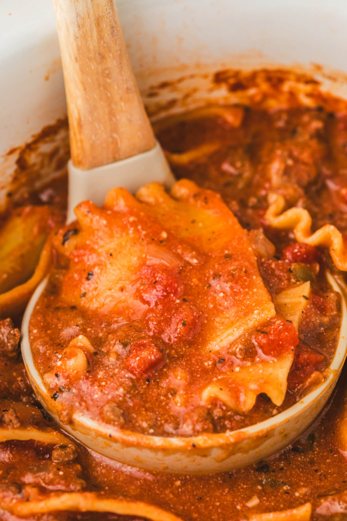 A ladle full of lasagna noodles in tomato soup broth.