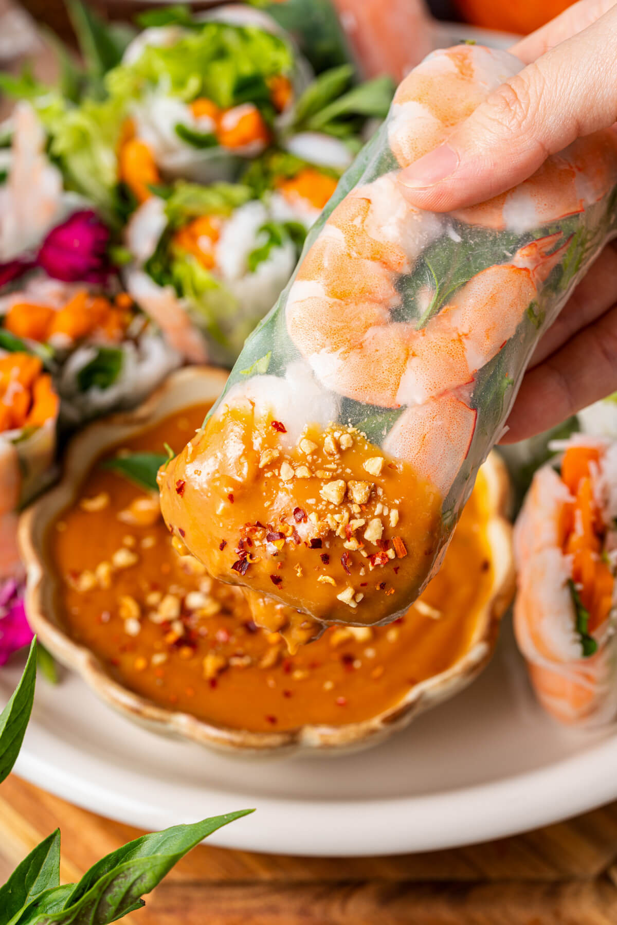 A hand dips a Vietnamese Shrimp Salad Roll into peanut sauce.