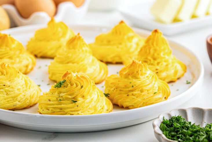 Golden baked swirls of rich baked Pommes Duchess on a white plate.