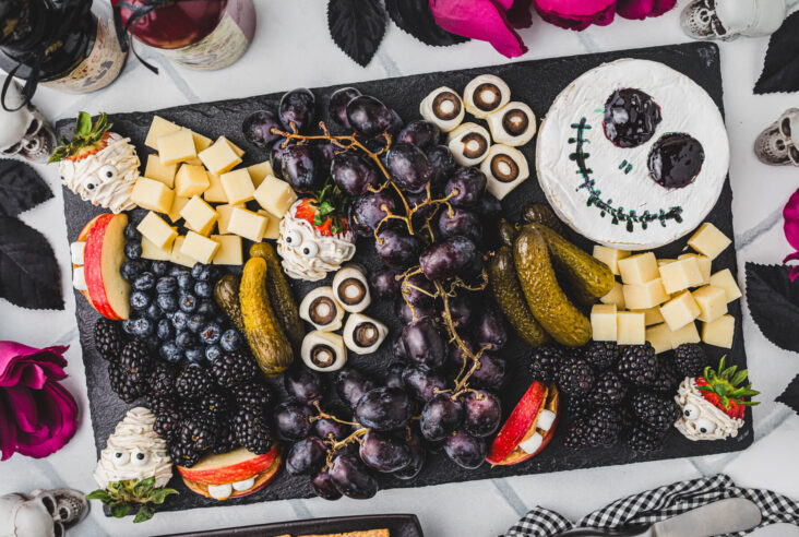 A Halloween party table containing a large charcuterie board featuring great ideas for spooky snacks.
