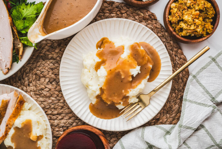 A white plate full of mashed potatoes covered in rich brown turkey gravy on a dinner table.