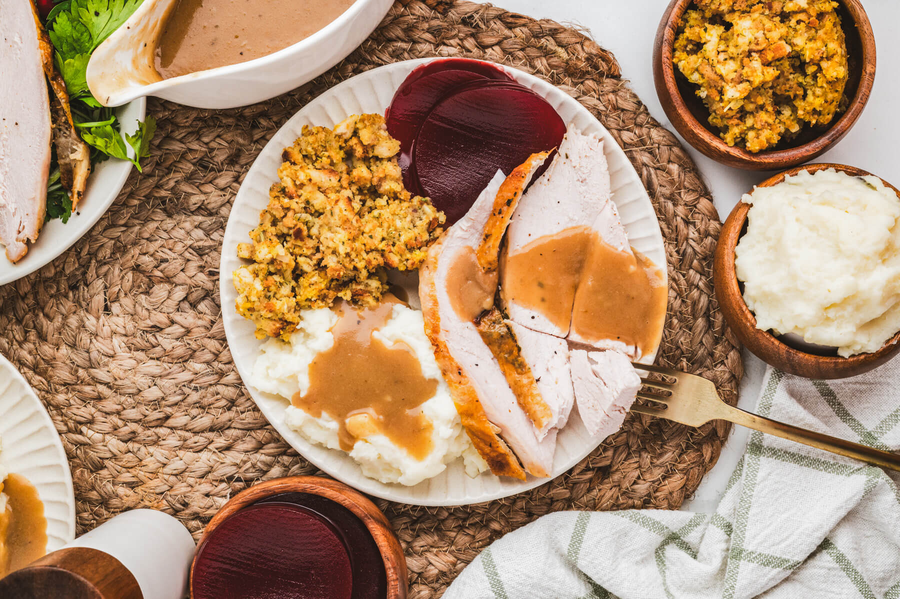 A plate of turkey dinner covered in homemade turkey gravy on a table filled with all the turkey dinner elements.