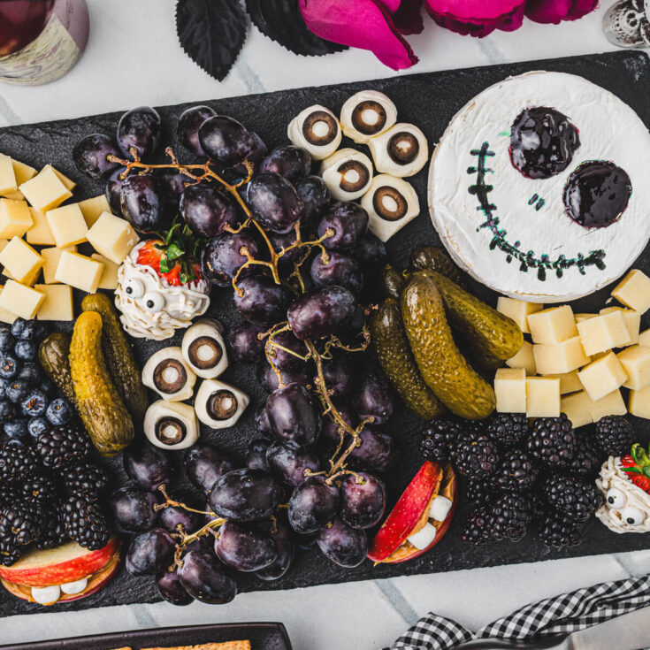 A Halloween party table containing a large charcuterie board featuring great ideas for spooky snacks.