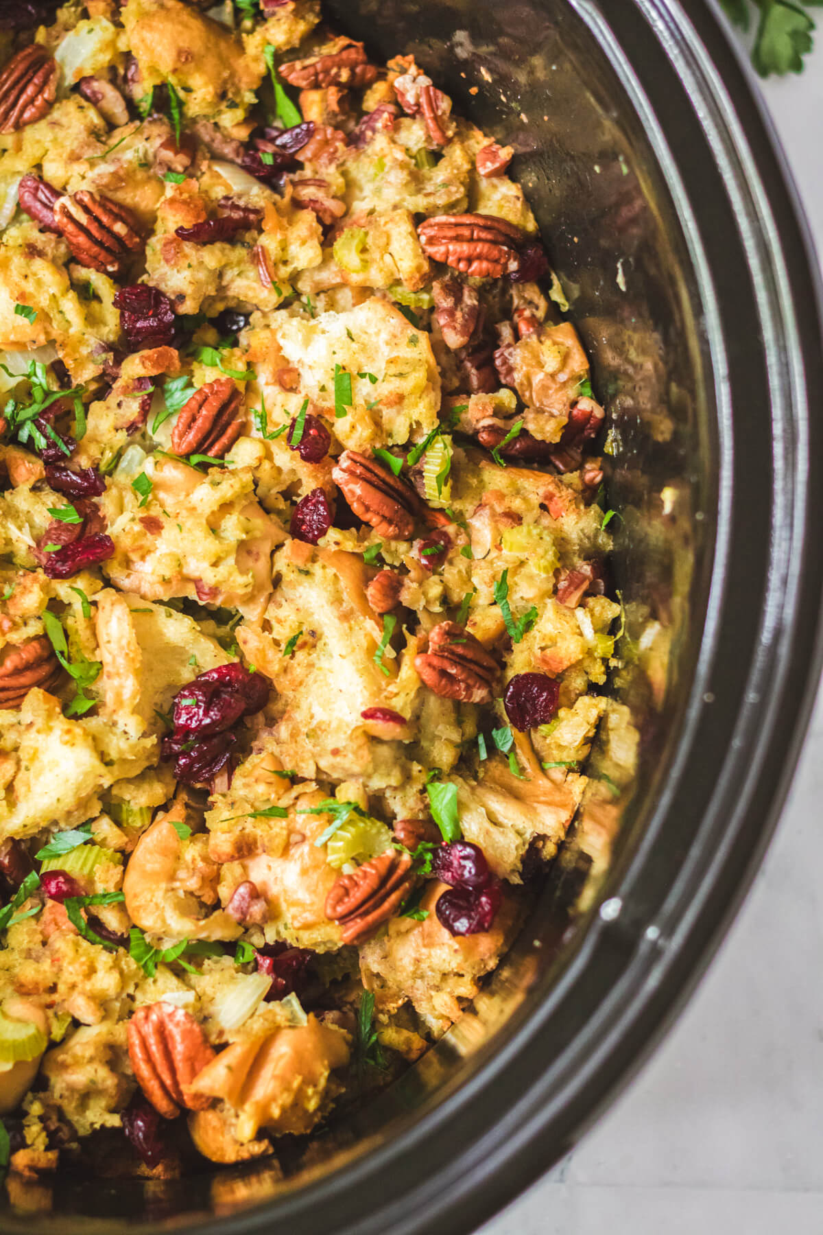 Slow Cooker Dressing in a black slow cooker with traditional bread dressing dotted with red dried cranberries, pecans, celery, and parsley.