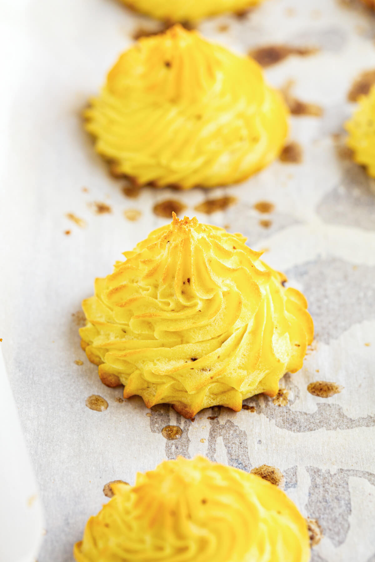 Three perfectly swirled golden brown baked Pommes Duchesse on a parchment paper lined baking sheet.