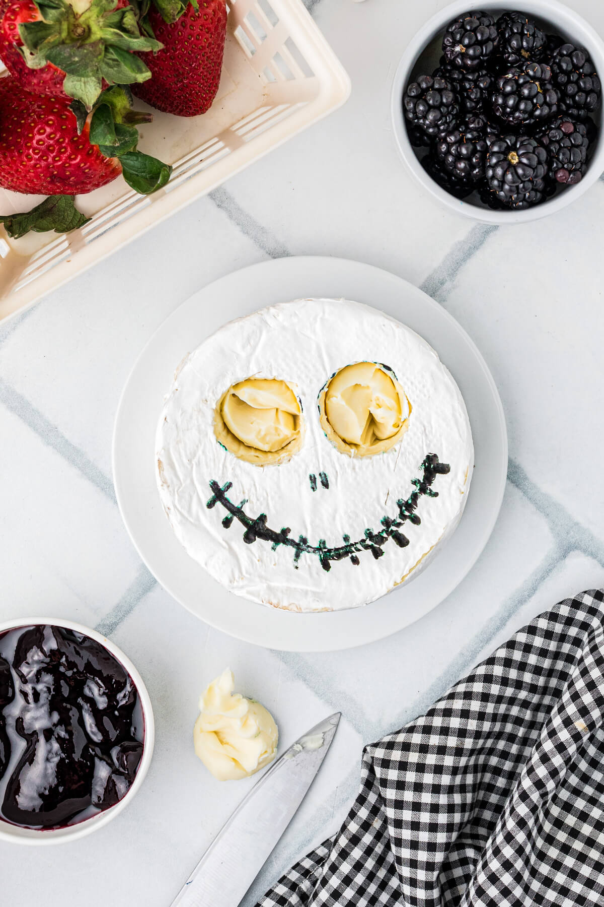 A photo showing how to hollow out the eye portions on a wheel of brie to make a Jack Skellington design.