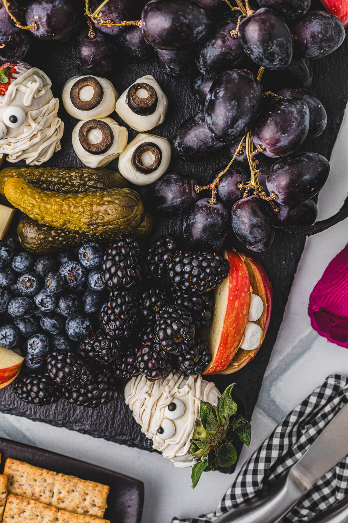 A Halloween party table containing a large charcuterie board featuring great ideas for spooky snacks.