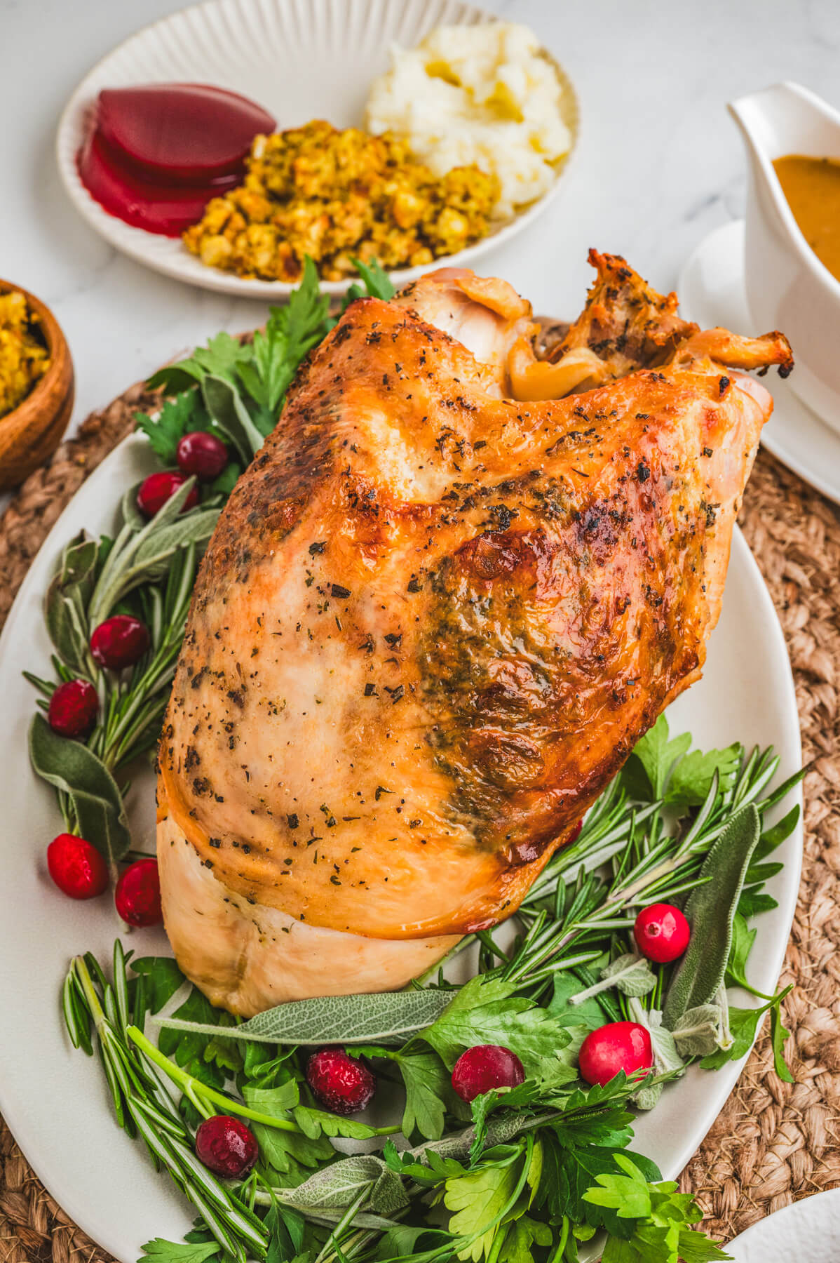 A golden brown crispy skin turkey breast on an oval platter surrounded by fresh herbs and cranberries.