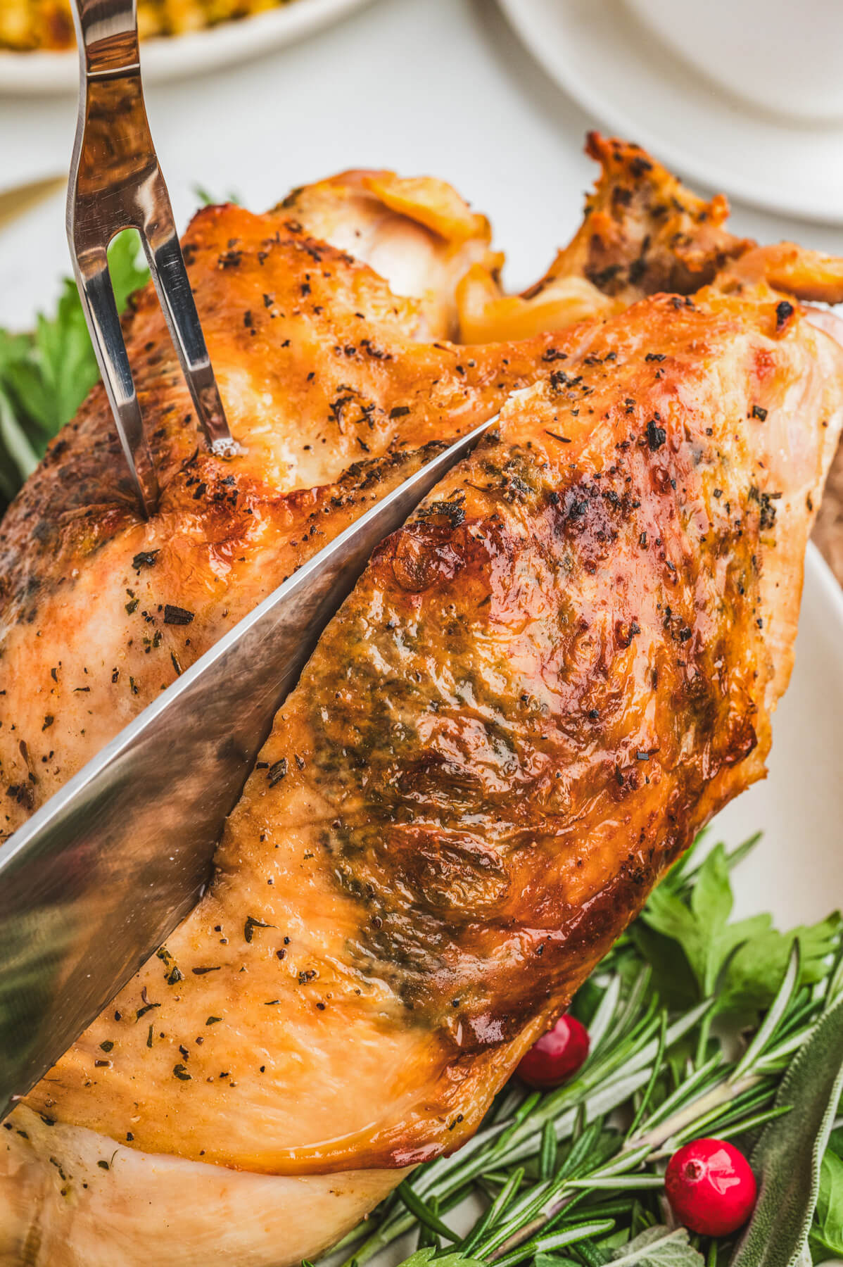 A carving knife and fork slicing into a golden brown turkey breast roast.