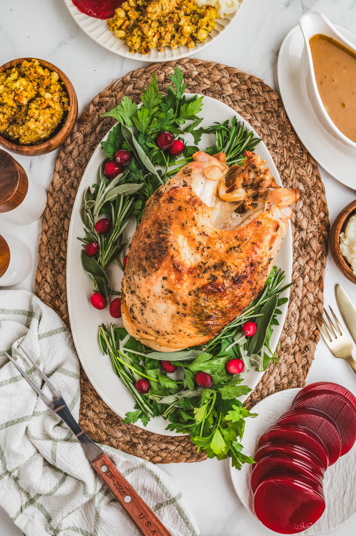 A golden brown crispy skin turkey breast on an oval platter surrounded by fresh herbs and cranberries.