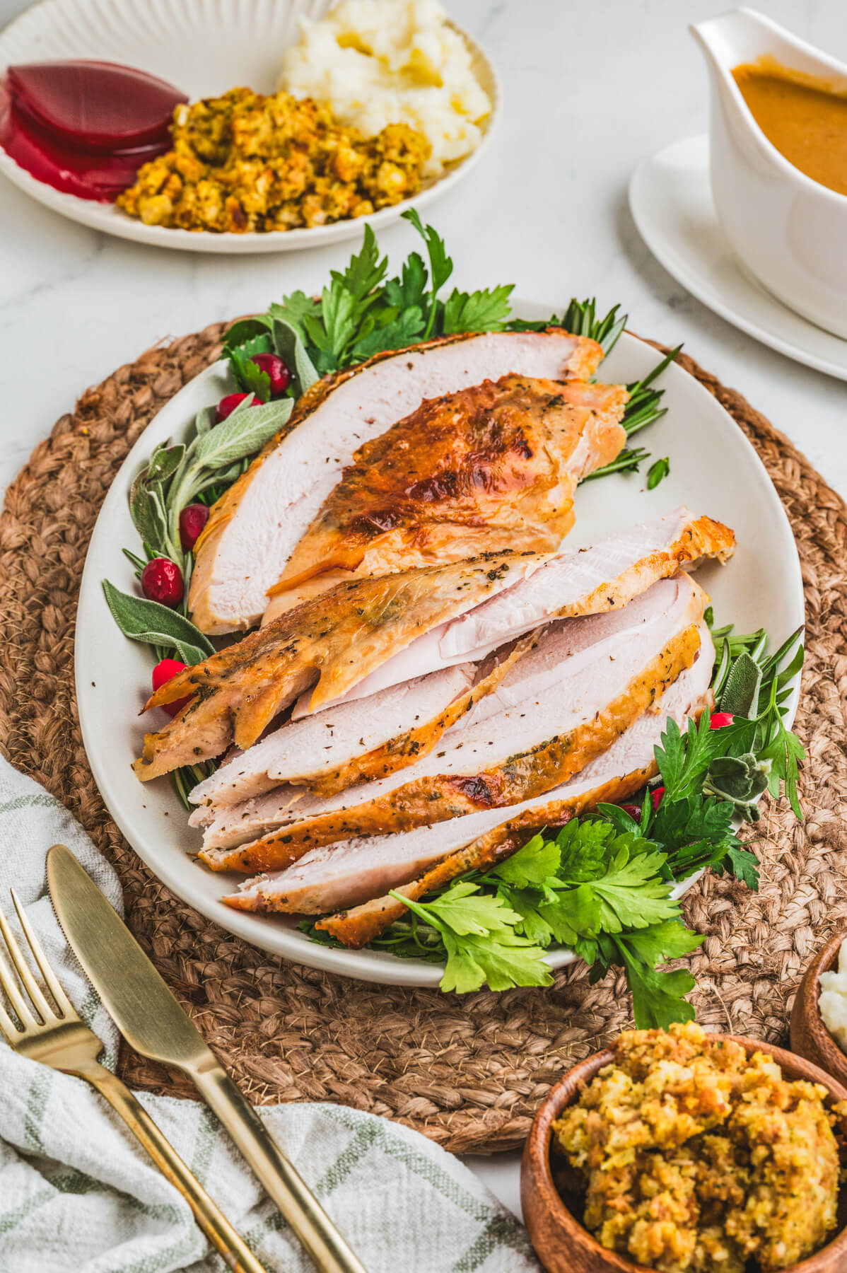 A sliced golden brown crispy skin turkey breast on an oval platter surrounded by fresh herbs and cranberries.