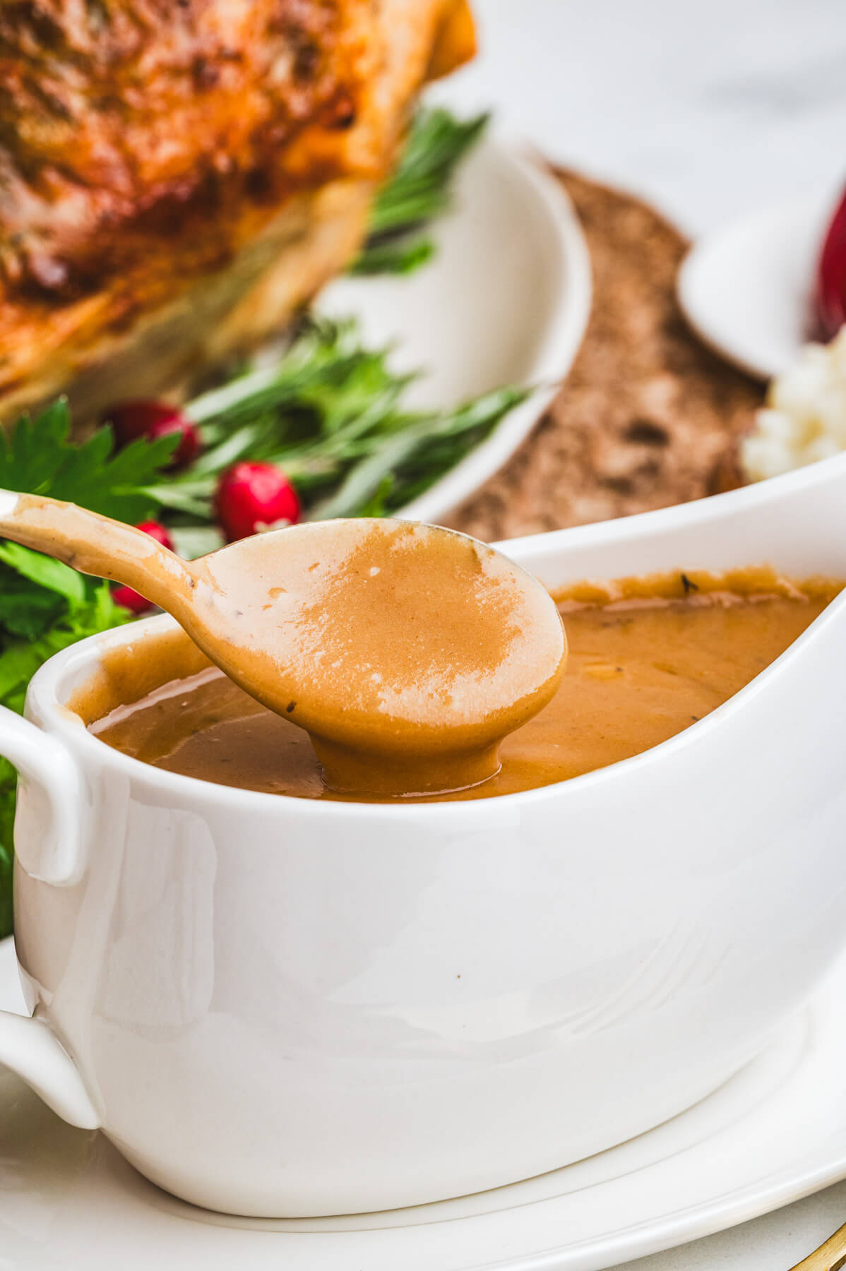 A spoon full of rich brown gravy drips over a white gravy boat.