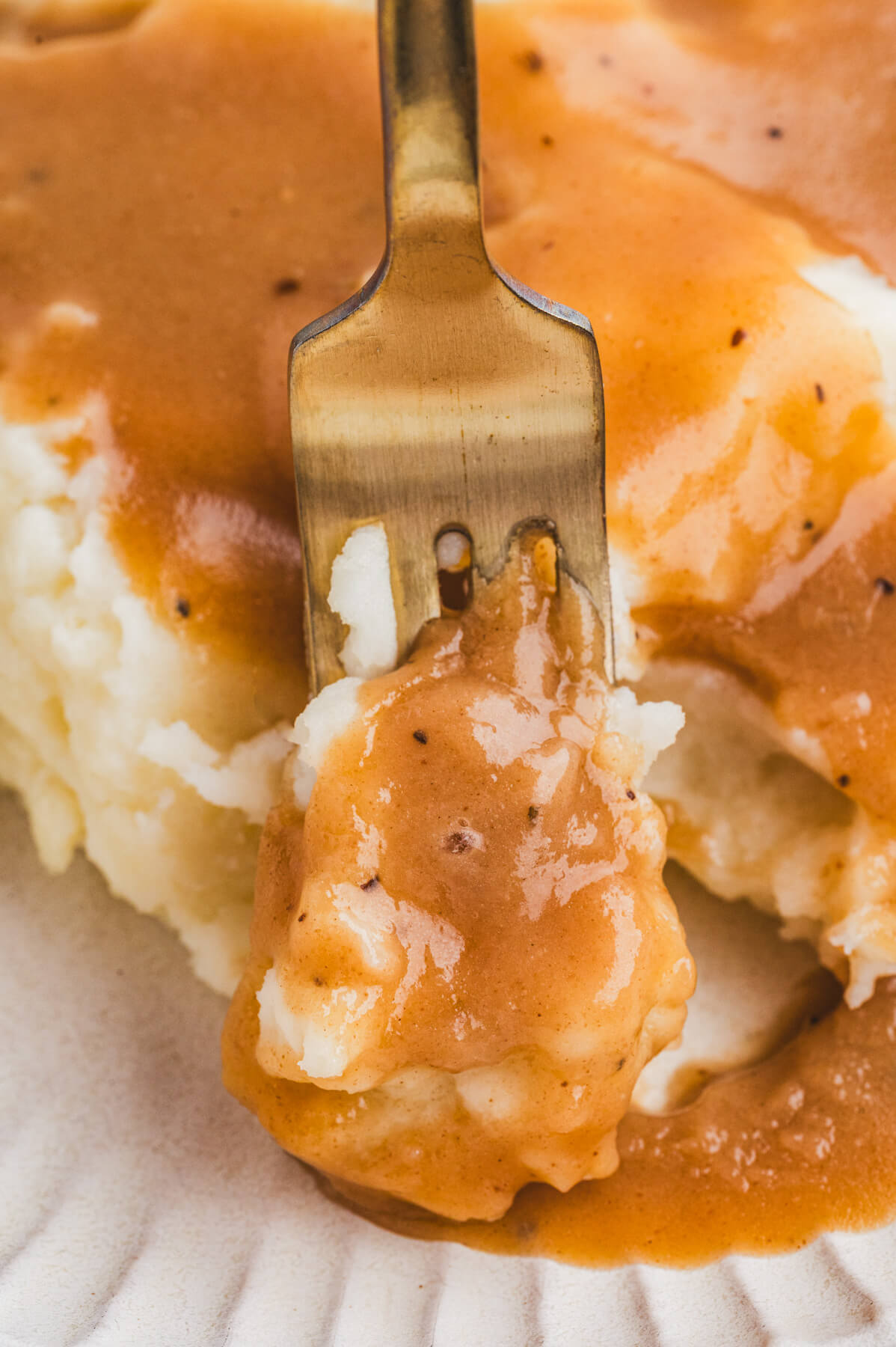 A fork digs into a pile of mashed potatoes covered in turkey gravy.