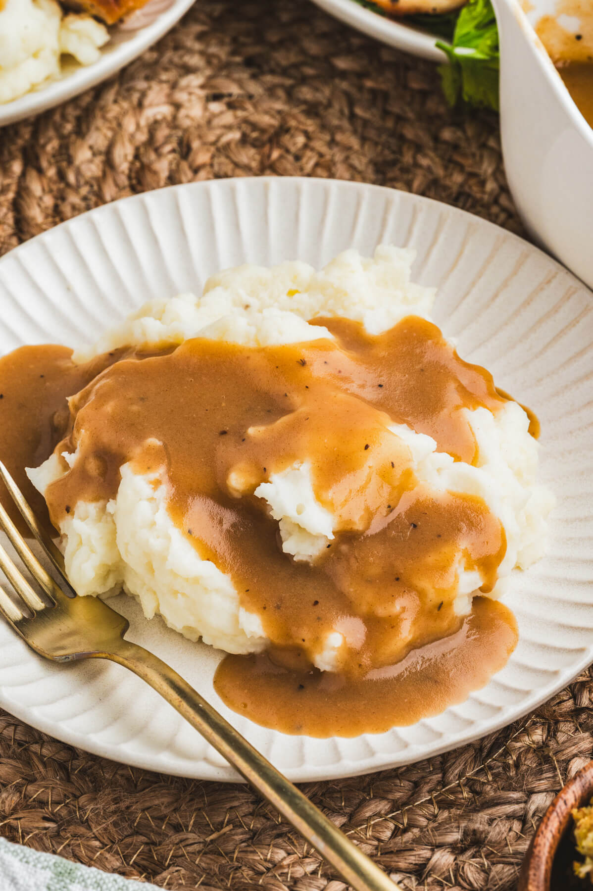 A white plate full of mashed potatoes covered in rich brown turkey gravy.