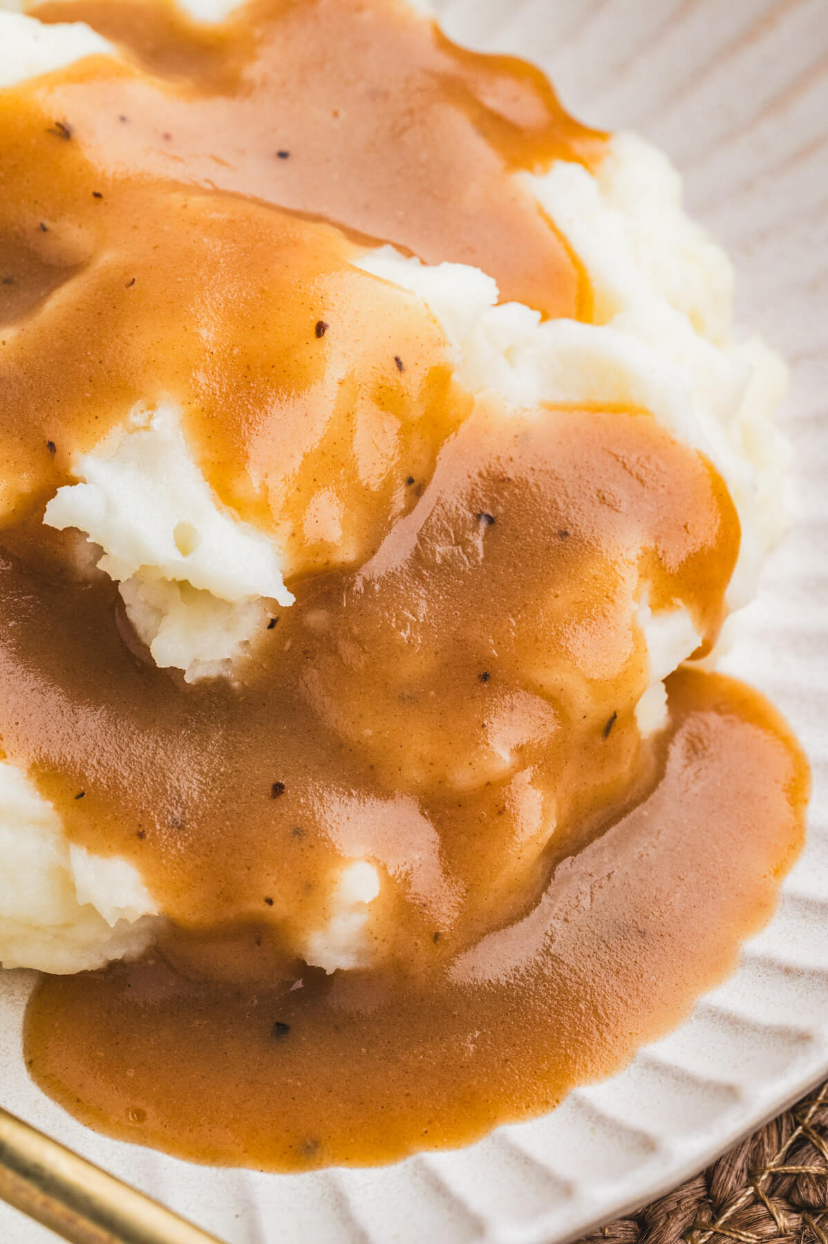 A white plate full of mashed potatoes covered in rich brown turkey gravy.