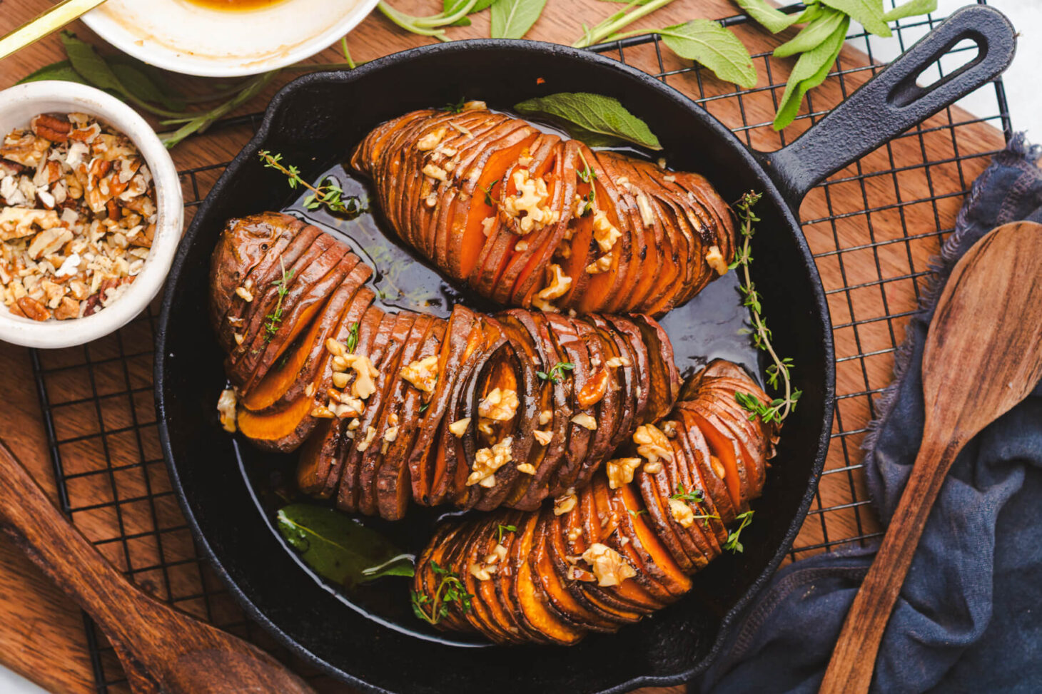 Three perfectly roasted vibrant orange hasselback sweet potatoes topped with herbs and walnuts in a cast iron pan.