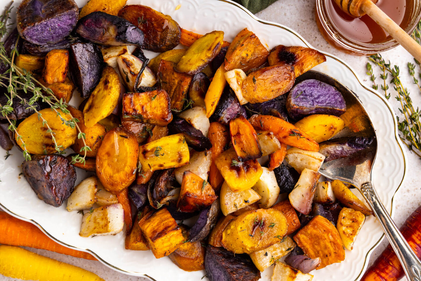 A white platter filled with colourful roasted root vegetables on a dinner table.