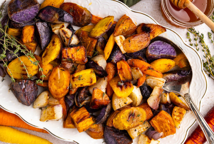 A white platter filled with colourful roasted root vegetables on a dinner table.