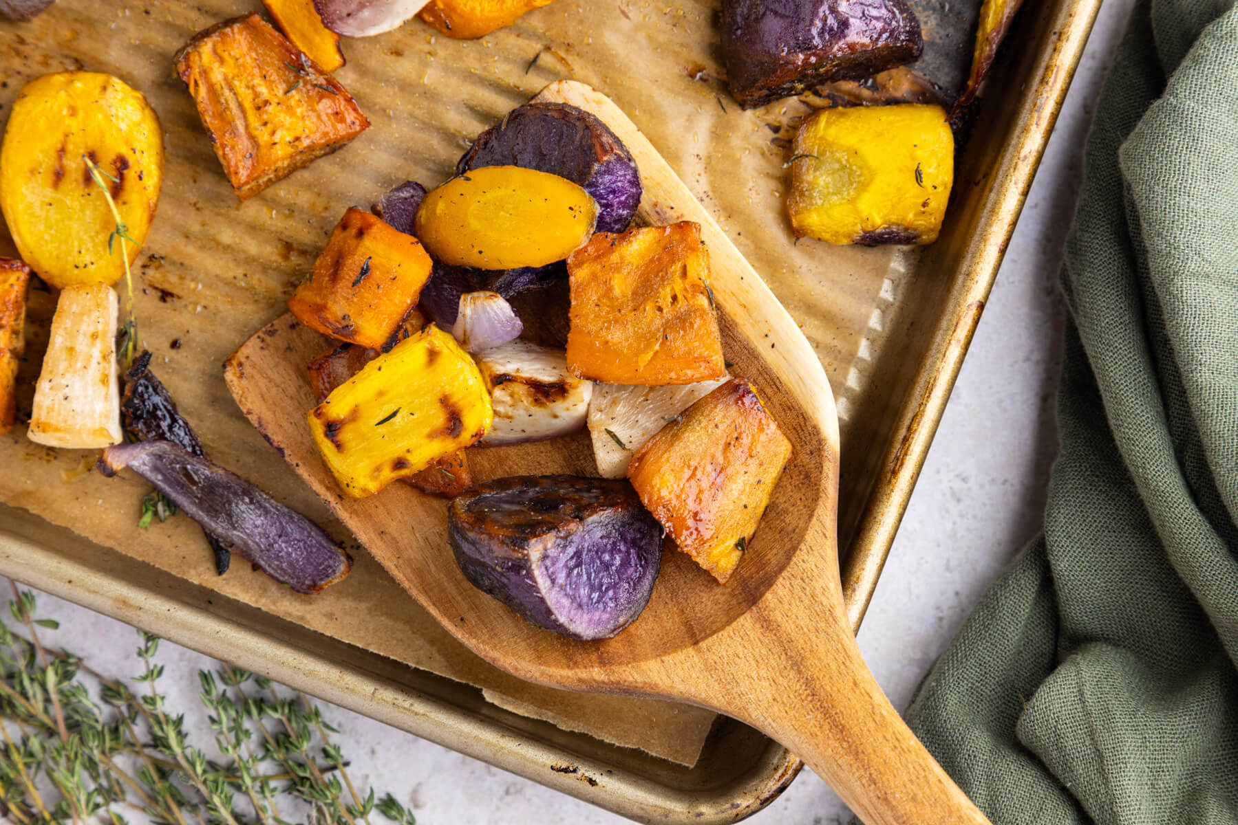 A wooden scoop holding a serving of colourful roasted root vegetables.