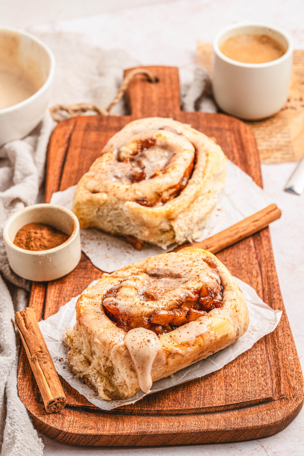 Two golden baked Apple Pie Cinnamon Rolls drizzled with frosting on a wooden serving board.