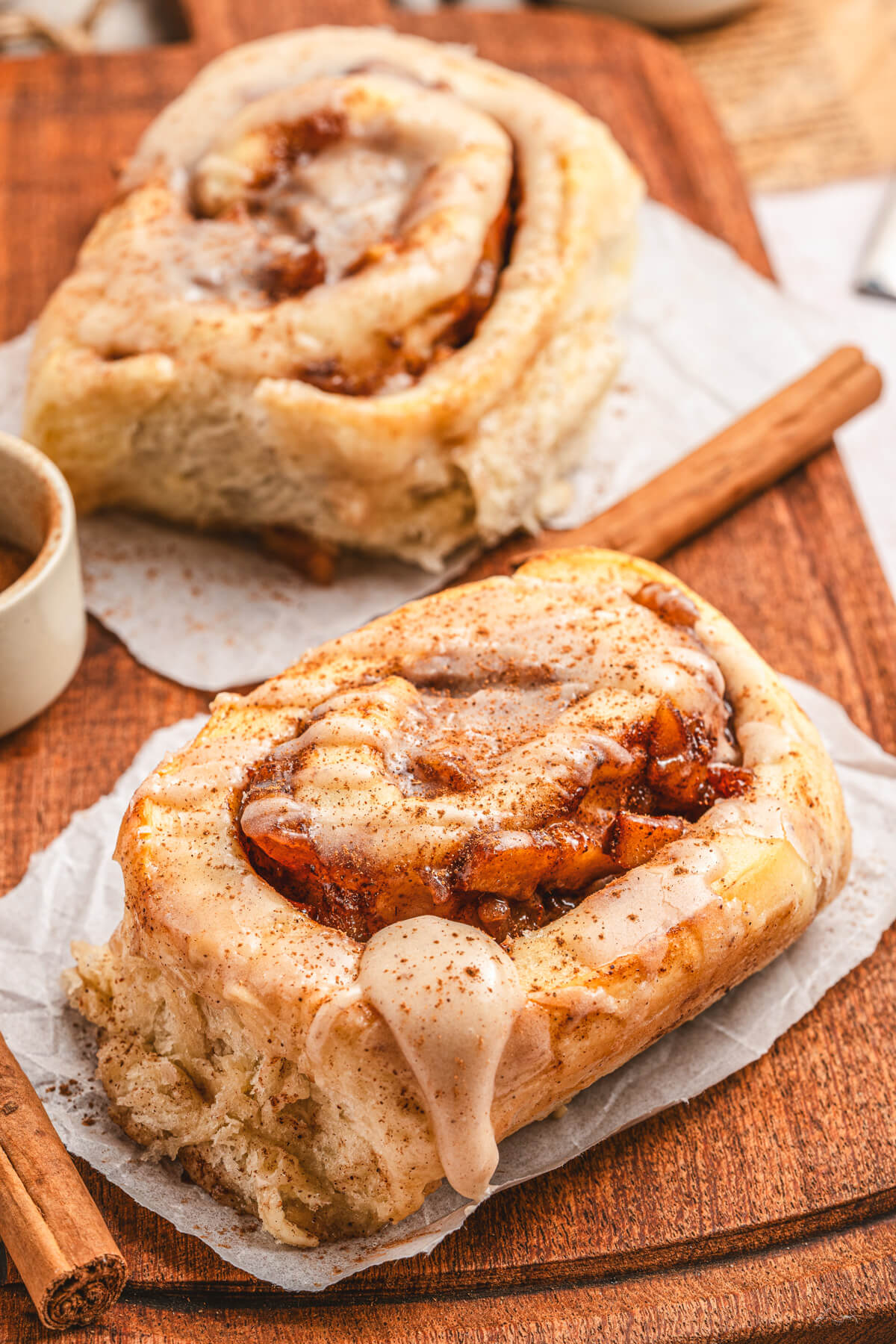 Two golden baked Apple Pie Cinnamon Rolls drizzled with frosting on a wooden serving board.