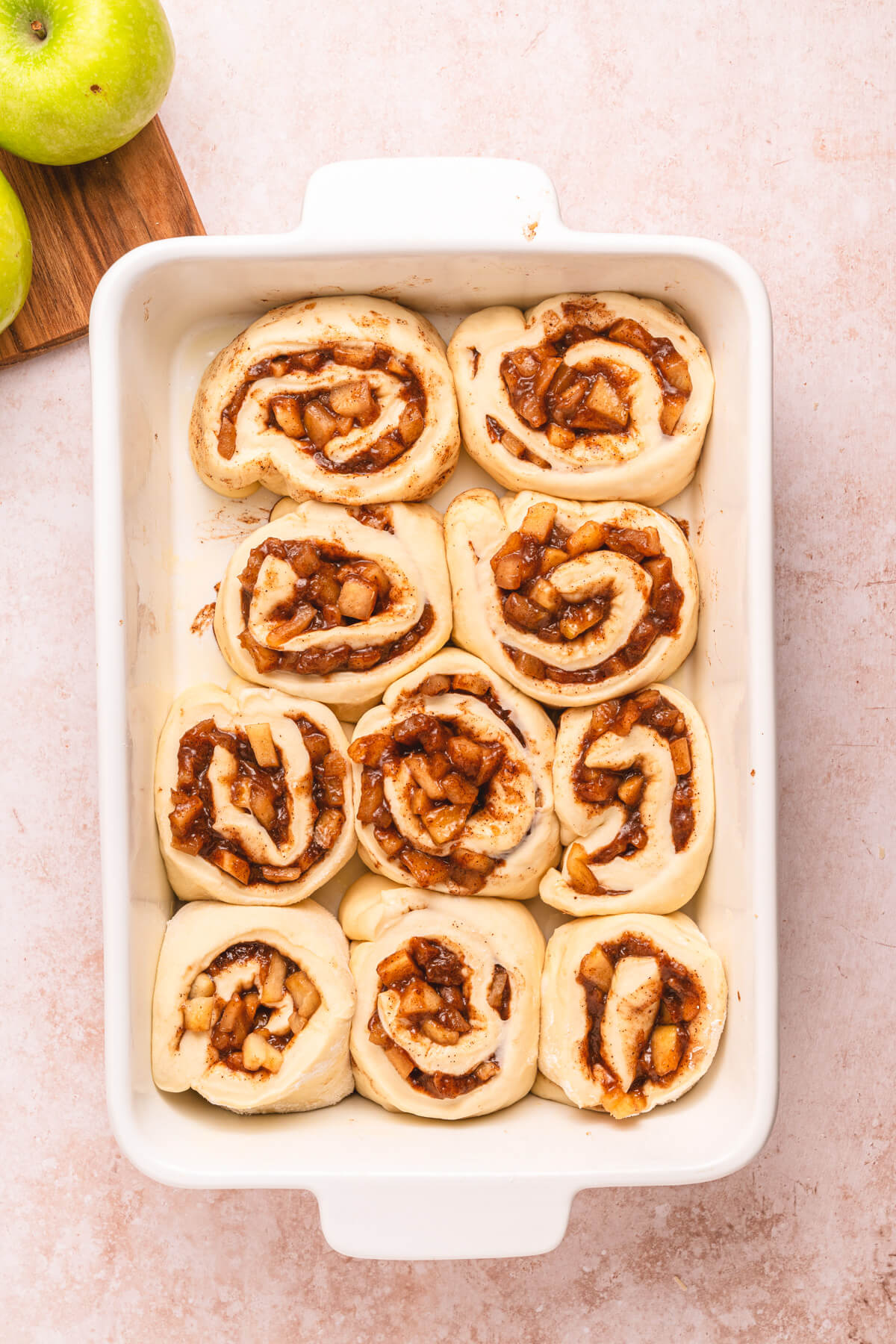 A white baking dish containing unbaked apple pie cinnamon rolls.