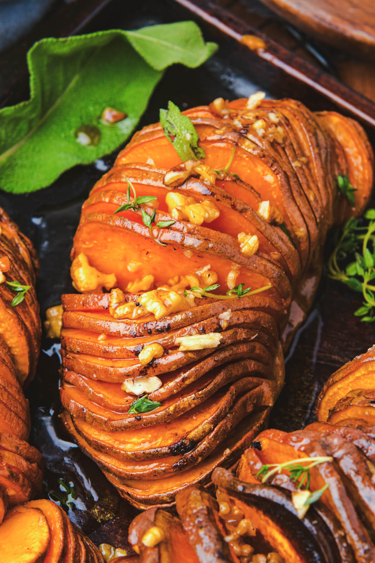 One perfectly roasted vibrant orange hasselback sweet potato topped with herbs and walnuts in a cast iron pan.