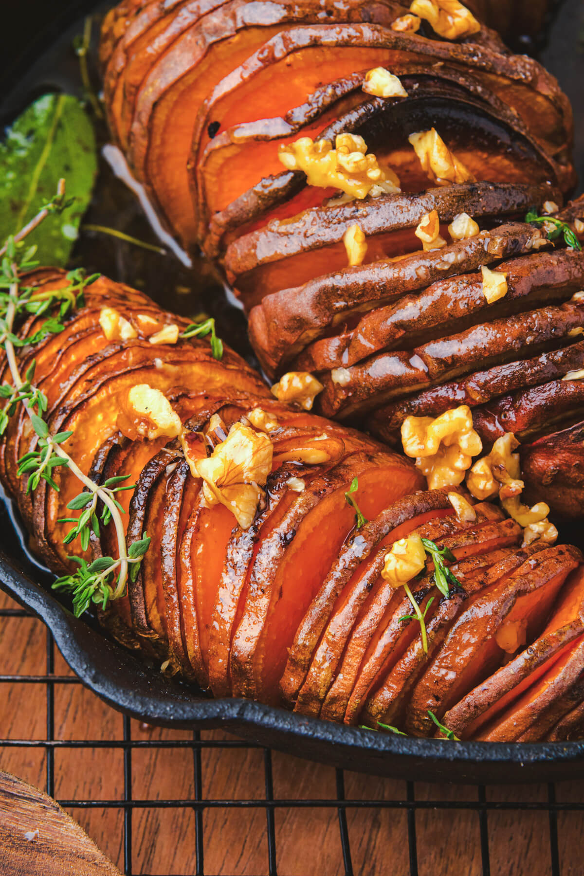 Two perfectly roasted vibrant orange hasselback sweet potatoes topped with herbs and walnuts in a cast iron pan.