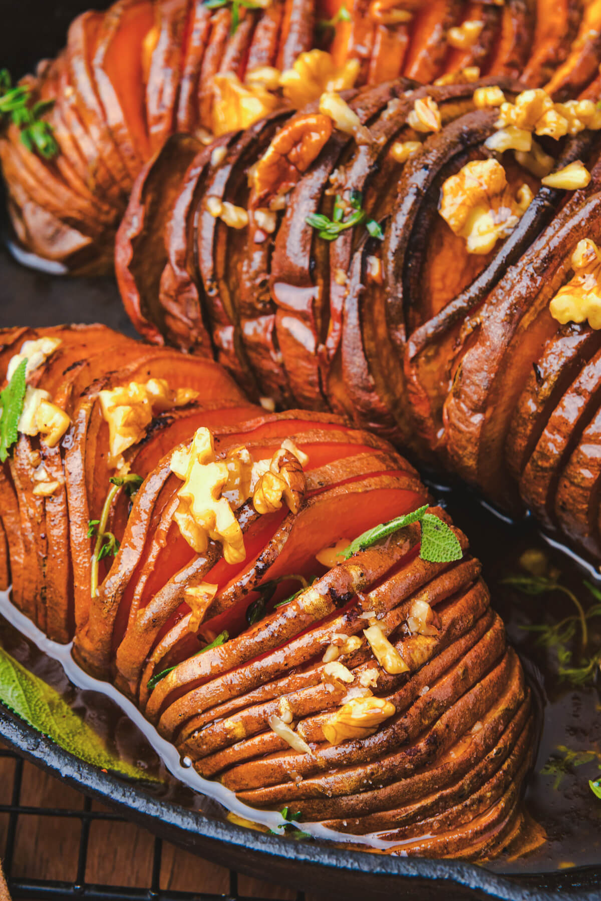 Two perfectly roasted vibrant orange hasselback sweet potatoes topped with herbs and walnuts in a cast iron pan.