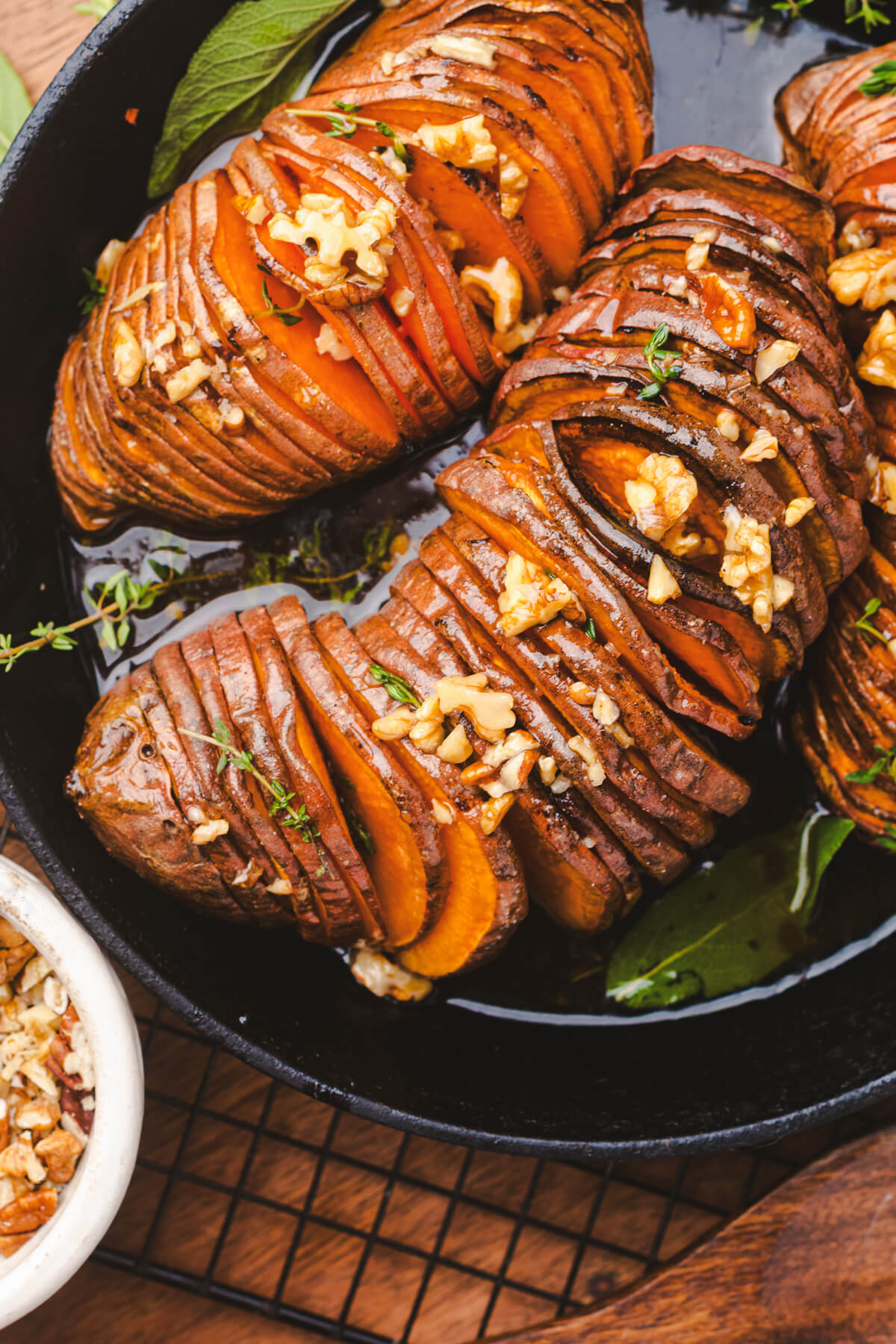 Two perfectly roasted vibrant orange hasselback sweet potatoes topped with herbs and walnuts in a cast iron pan.