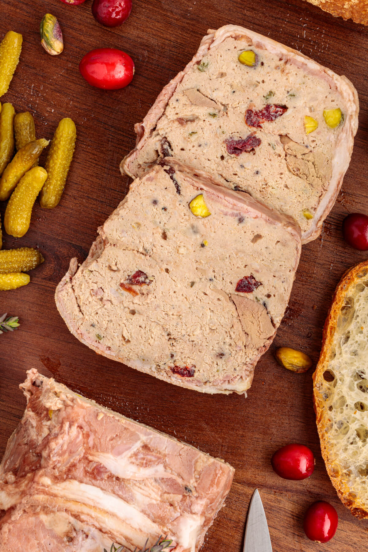 Slices of bacon wrapped pork terrine dotted with dried cranberries and green pistachios on a cutting board.
