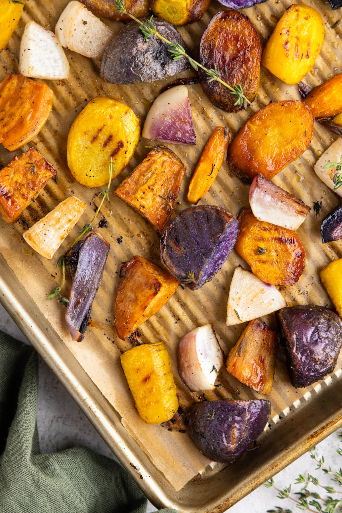 A parchment lined baking tray filled with colourful caramelized roasted root vegetables.