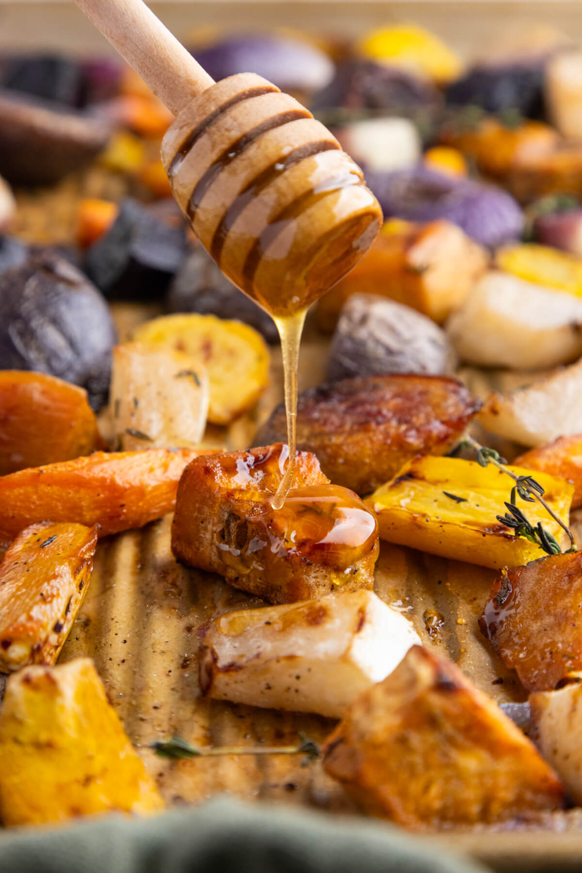 Colourful roasted root vegetables on a white platter being drizzled with honey