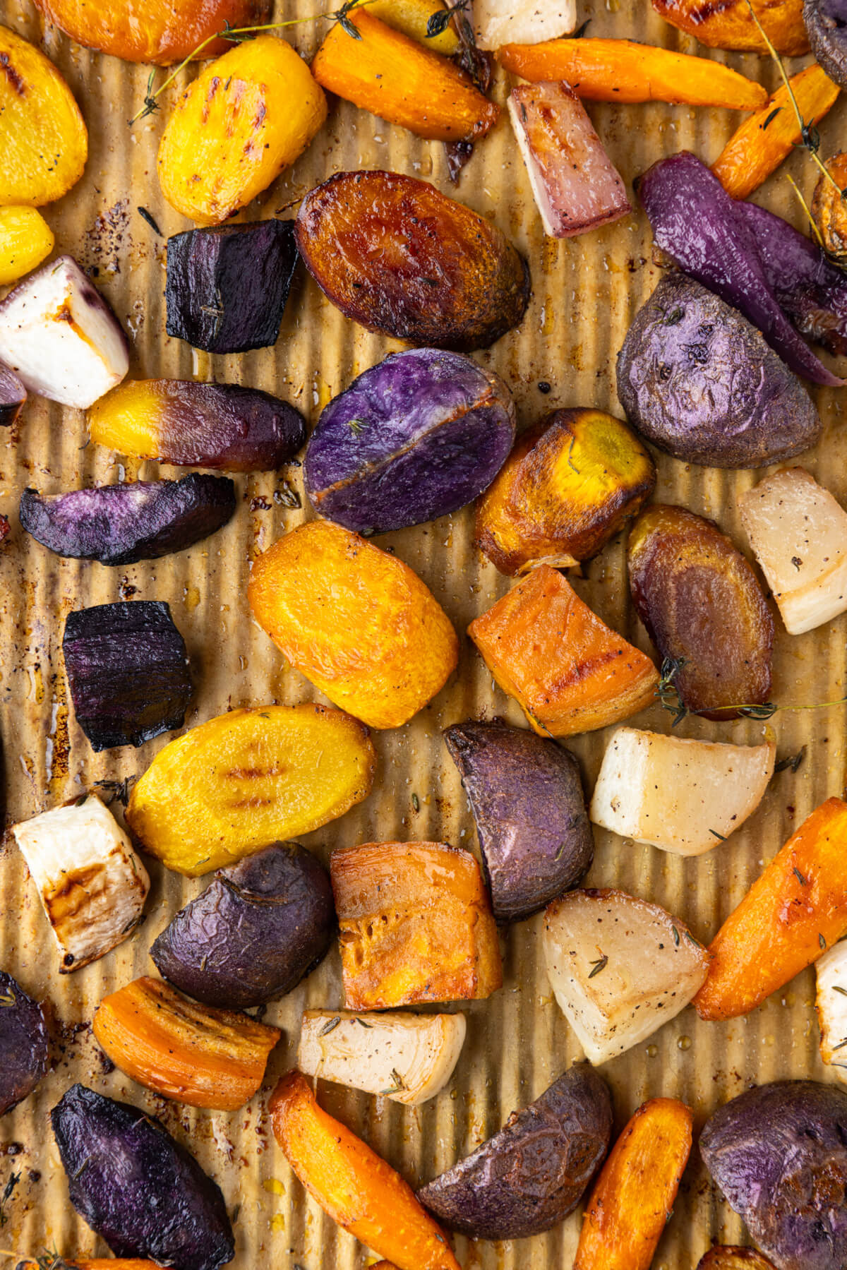 A parchment lined baking tray filled with colourful caramelized roasted root vegetables.